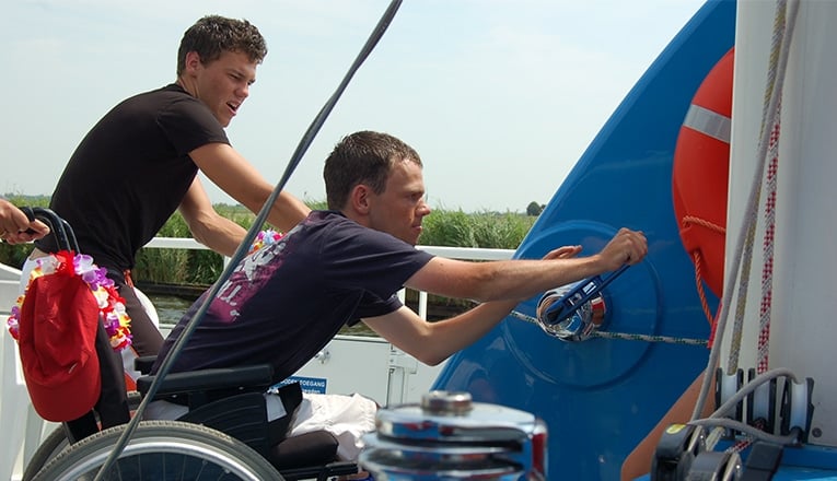 Twee deelnemers aan een watersportvakantie van SailWise zijn aan het zeilen op de voor mindervaliden aangepaste catamaran Beatrix. Foto: Hans Larkens.