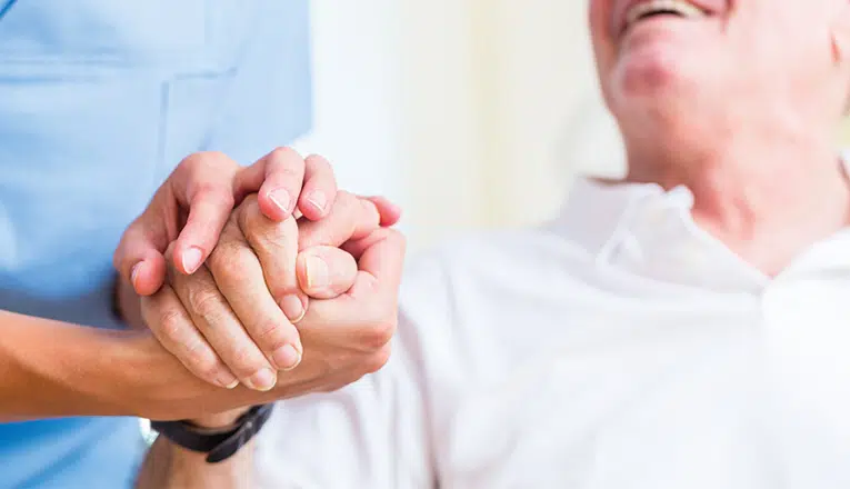 Meneer met dementie houdt de hand vast van een verzorger