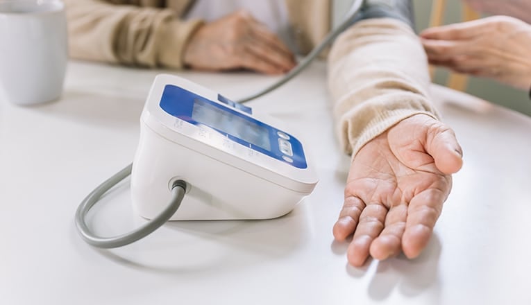 Een oudere vrouw gebruikt een bloeddrukmeter; een hulpmiddel om de bloeddruk in de gaten te houden.
