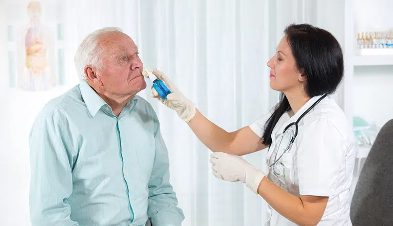 Vrouwelijke dokter helpt een oudere meneer met de neusspray