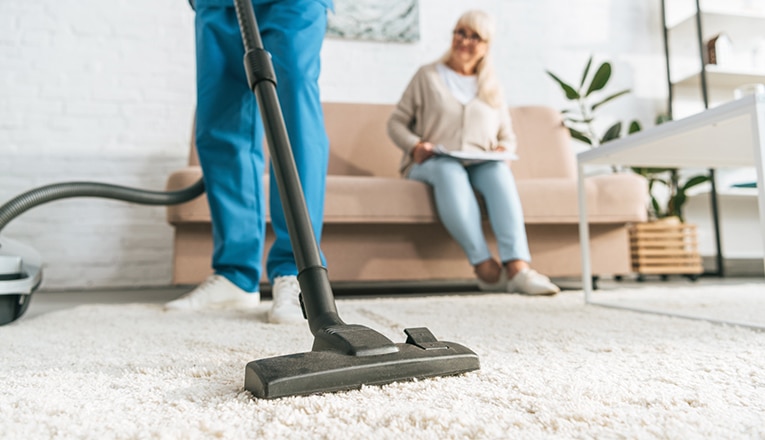 Een thuiszorgmedewerker stofzuigt de woning van een oudere als onderdeel van ouderenzorg aan huis.