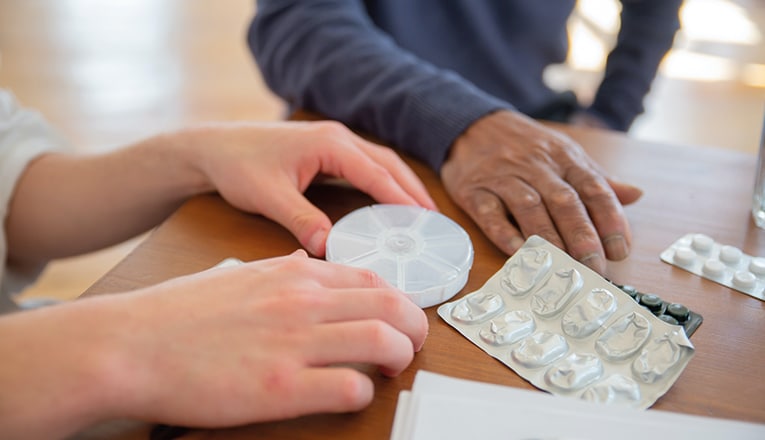 Een hulpverlener geeft een oudere in een verpleeghuis zorg door te helpen met de dagelijkse medicatie.