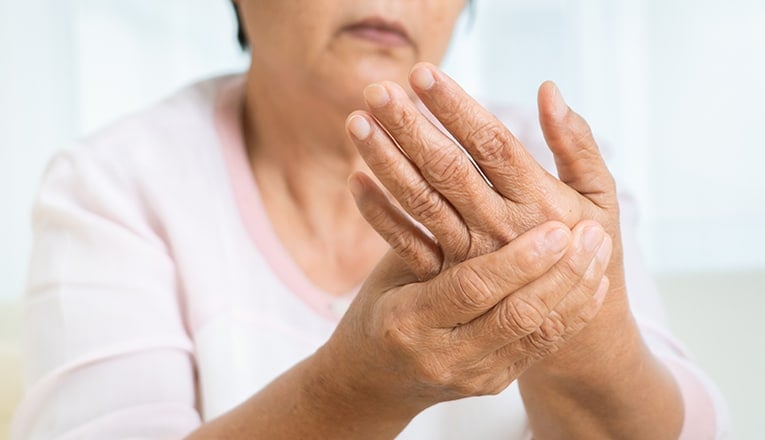 Een oudere vrouw ervaart pijn van de reuma in haar handen.