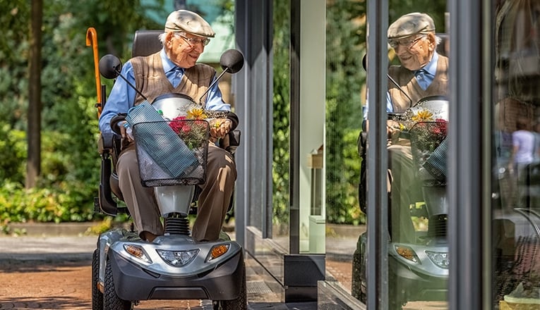 Een seniore man maakt gebruik van een hulpmiddel, een scootmobiel, om zelfstandig te kunnen winkelen.